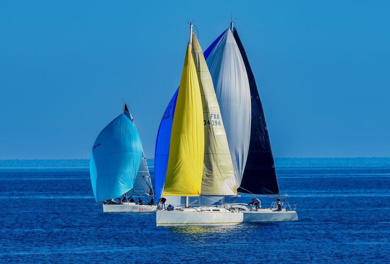 Three vibrant sailboats competing in a sailing race on the open sea under a clear blue sky.