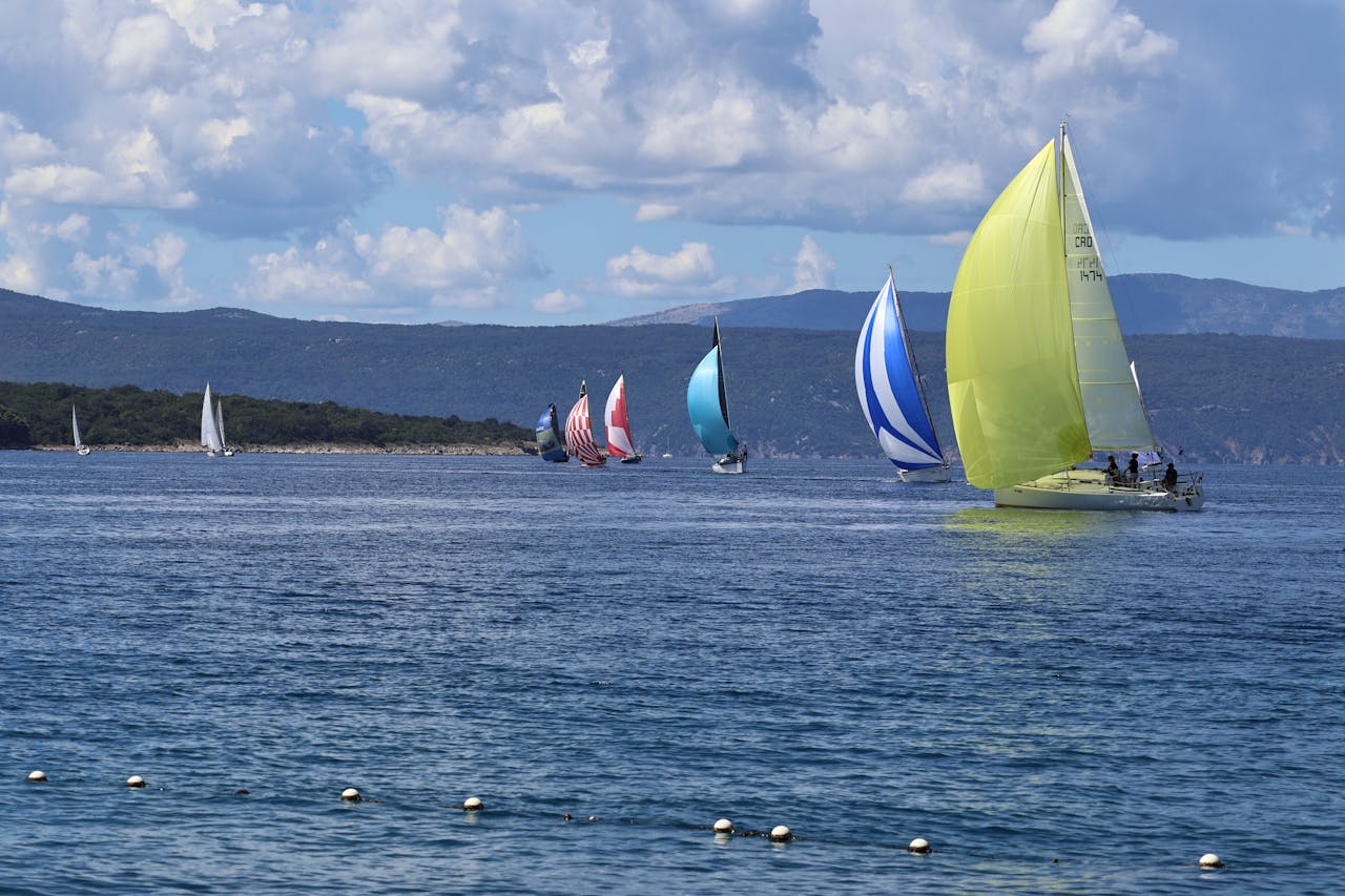 Vibrant sailboats compete in a scenic ocean race under a cloudy blue sky.
